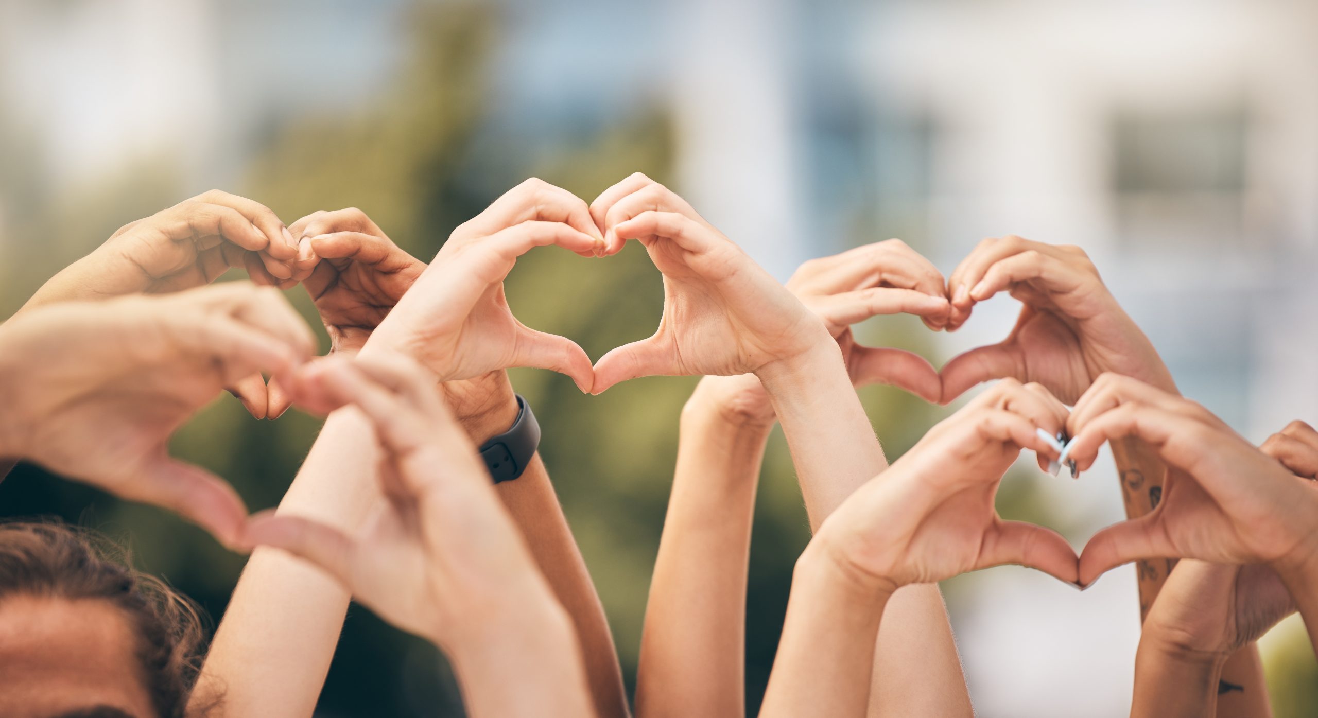 Hand, heart and love with a group of people making a sign with their hands outdoor together in the day. Crowd, freedom and community with man and woman friends doing a gesture to promote health.